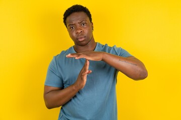 Young handsome man standing over yellow studio background being upset showing a timeout gesture,...