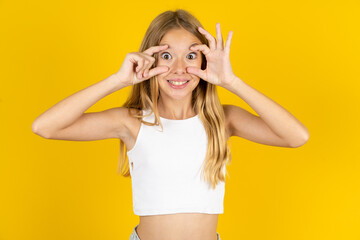 young beautiful teen girl standing over yellow studio background keeping eyes opened to find a...