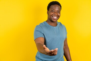 Young handsome man standing over yellow studio background smiling cheerful offering palm hand...