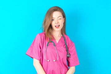 beautiful doctor woman standing over blue studio background  winking looking at the camera with...