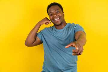 Young handsome man standing over yellow studio background smiling cheerfully and pointing to camera...