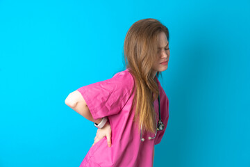 Beautiful doctor woman wearing pink medical uniform over blue background Suffering of backache,...