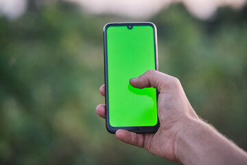 Smart farming, technology and gardening. Farmer or gardener holding smartphone with green screen while working in garden, using mobile app in farming