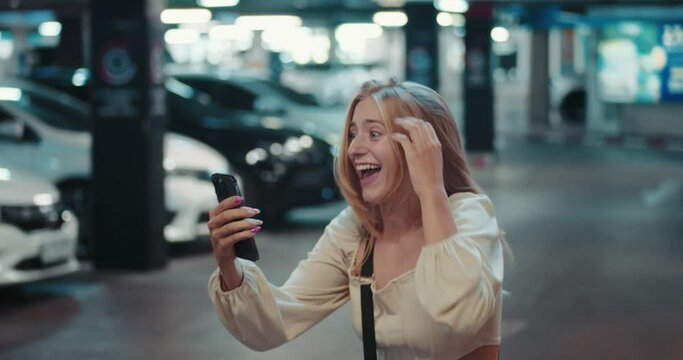 female student standing in a parking lot holds a smartphone reads good news. concept of victory. female student shouts yes rejoices in victory. excited woman shows positive emotions of joy, victory