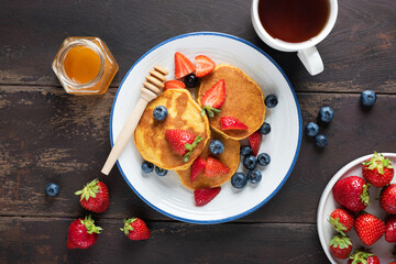Pancakes with honey and berries and cup of tea on a wooden table background, top view. Sweet healthy breakfast or lunch meal