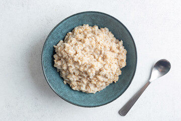 Cooked oatmeal porridge, irish steel cut oats without toppings. Top view on grey concrete table background, copy space