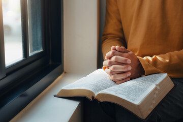 A man hands folded holy bible by the window in library and church