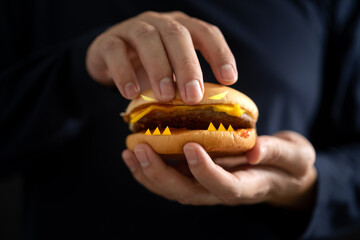 Man's hand holding a hamburger with monster teeth, concept of horror and danger hidden by fast food...