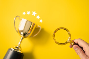 Man's hand is holding a magnifying glass and a golden trophy lies on a yellow background. , the concept of finding success