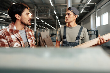 Two young carpenters working with wood standing at table in workshop