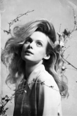 Woman with big wavy hair studio portrait. Model surrounded with flower twigs with blossoms. Retro vintage style with grain, noise, blur and grunge texture effect applied. Black and white image