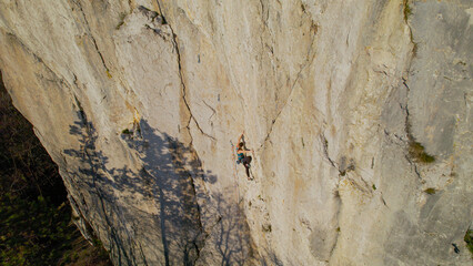 AERIAL: Fit young woman climbing a difficult route in broad limestone cliff