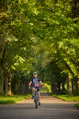 attractive senior woman cycling with her electric mountain bike in a beautiful old oak tree and chestnut avenue in Ludwigsburg, Baden-Wuerttemberg, Germany
