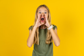 Beautiful caucasian kid girl wearing green dress shouting excited to front.