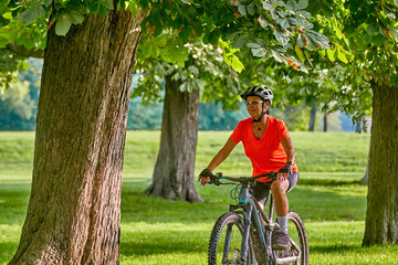 attractive senior woman cycling with her electric mountain bike in a beautiful old oak tree and...