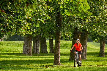 Fototapeta na wymiar attractive senior woman cycling with her electric mountain bike in a beautiful old oak tree and chestnut avenue in Ludwigsburg, Baden-Wuerttemberg, Germany 