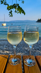 Two glasses of wine filled with white house wine, placed on a wooden table by the beach in Medveja,...