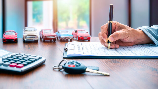Man signing contract on car loan application form. Car loan or buying a new car concept. Miniature cars and car key on table. 