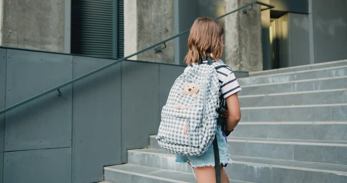 Student school girl with books walking up stairs to the modern campus building. Concept of learning and lifestyle in teens life.