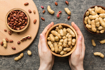 Woman hands holding a wooden bowl with close peanuts. Healthy food and snack. Vegetarian snacks of different nuts
