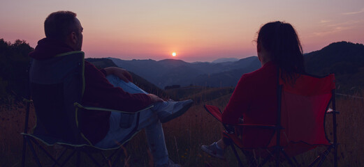 Man and woman looking at the sunset over the distant mountains.