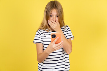 Beautiful caucasian kid girl wearing striped  T-shirt being deeply surprised, stares at smartphone display, reads shocking news on website, Omg, its horrible!