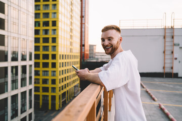 Smiling man with smartphone standing on terrace