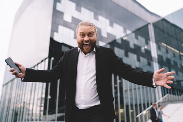 Excited businessman with smartphone on street