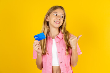 Beautiful caucasian kid girl wearing pink shirt hold credit card point empty space