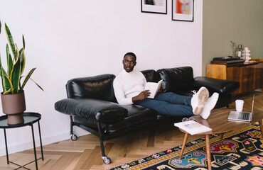 Pensive African American man with legs on table and book