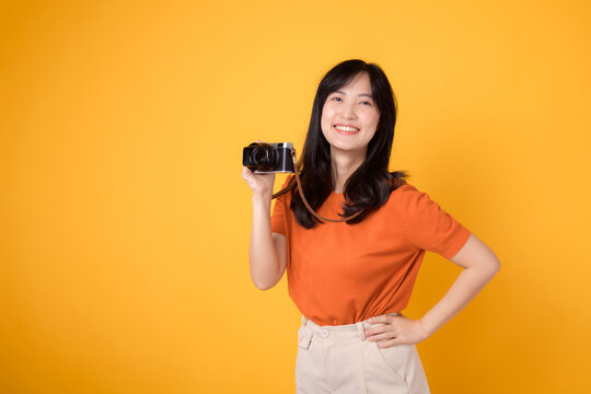 Personable young woman with a camera isolated on yellow background, capturing the essence of a happy vacation traveler.