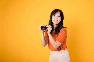 Obraz premium Excited woman traveler capturing her holiday memories with a camera isolated on yellow background. Adventure concept.