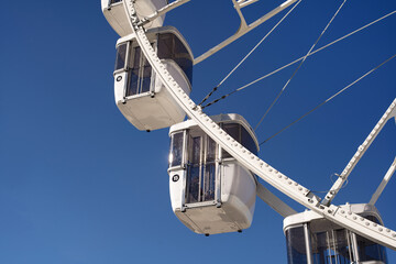 modern ferris wheel with closed cabins at carnival with blue sky no clouds in the background illuminated wide angle close up shot