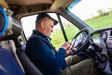 Mature truck driver using mobile phone while driving transport vehicle.