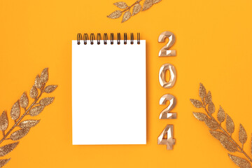 Blank notepad mockup, glittering decorative branches and 2024 golden numbers on a yellow background. New Year goals list concept.