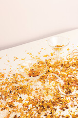 Small crystal glasses and golden glittering confetti in front of beige background. Festive creative concept.