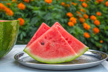 On a tray are several slices of watermelon in the shape of a triangle, in the background are summer orange flowers.