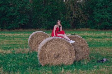Girl in a red dress near a round bale of straw