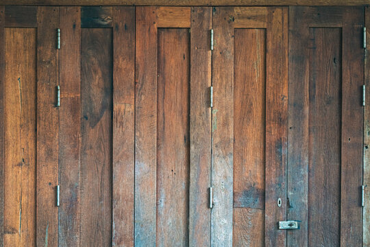 Traditional antique wooden folding door Asian style frame. Thai traditional wooden gate of historical architecture. Beautiful retro wooden folding door with lock under evening sunlight. Vintage Door.