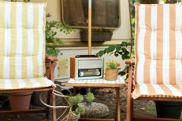 The FM channel is playing music, a stylish retro radio player stands on a wooden table. Wooden deckchair near Campsite on caravan or camper van. Lounge sunbed.  Brown vintage radio