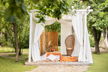 Outdoor design of arbour. Rattan peacock armchair and decorative folding screen divider. Summer gazebo with flowing white curtains. Wedding boho decoration. Decor outdoor terrace with wicker furniture © stock_studio