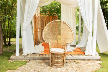 Rattan peacock armchair and decorative folding screen divider. Summer gazebo with flowing white...