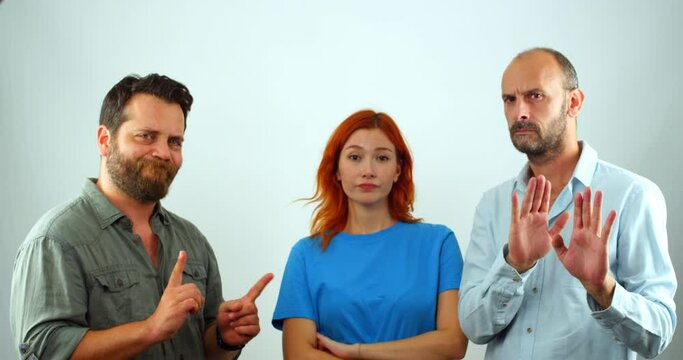A group of coworkers, a woman and two men, looking at the camera. They are clearly disapproving of something, as they are all shaking their heads and making hand gestures that mean "no"
