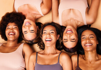 Diversity, beauty and portrait of women from above with smile, self love and solidarity in studio. Happy face, group of friends on beige background with underwear, skincare and cosmetics on floor.