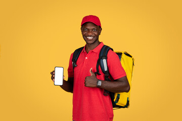 Cheerful millennial african american guy courier with backpack show phone with empty screen, thumb up