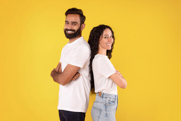 Happy middle eastern couple posing back to back, yellow background