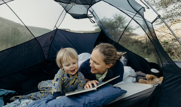 A mother reads a book to her young toddler son inside a tent during a camping trip in Oregon.