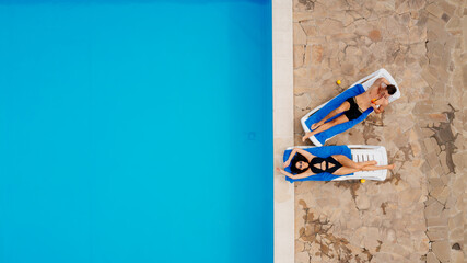 A couple in love, a man and a young woman, lie on sun loungers near the pool, enjoy a tropical vacation and each other's company. View from above.