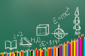 multicolored pencils on green chalkboard background, copy space, back to school concept and growth to knowledge, formulas, numbers, drawings, geometric shapes