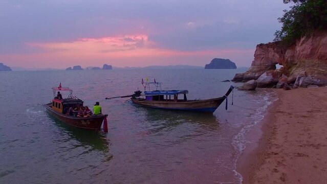 Long-tailed boats are waiting for tourists to visit the strangely shaped cape..The cape is pink in color with a large hollow in sweet sunset..stunning pink sunset above the ocean.